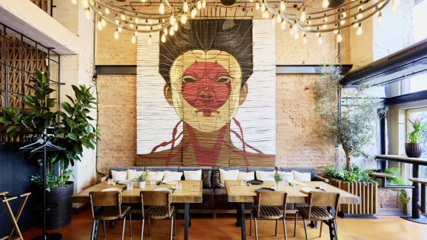 Ein Restaurant mit Holztischen, Stühlen und einem großen Wandbild einer Person.