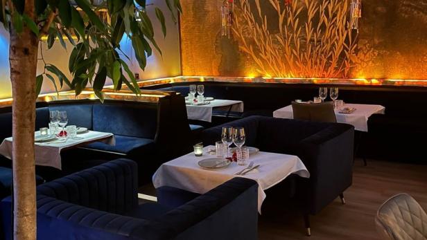 Ein elegant eingerichtetes Restaurant mit blauen Samtsesseln und einem Wandgemälde.