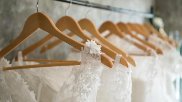 Mehrere weiße Brautkleider hängen an hölzernen Kleiderbügeln.