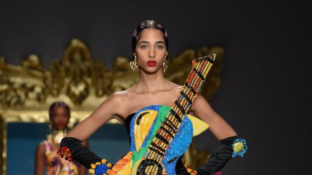 Ein Model präsentiert ein farbenfrohes Kleid in Gitarrenform auf einem Laufsteg.