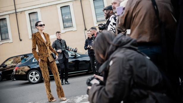 Eine Frau in einem braunen Anzug wird von Fotografen auf der Straße fotografiert.