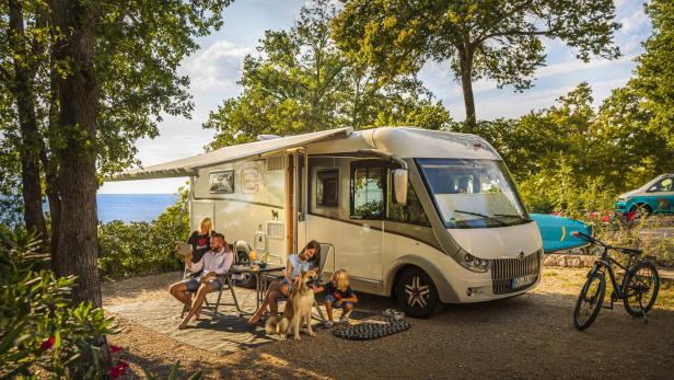 Eine Familie entspannt mit Hund vor ihrem Wohnmobil auf einem Campingplatz in Küstennähe.