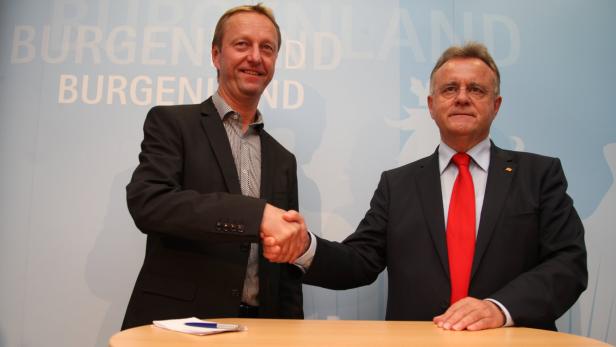 Zwei Männer in Anzügen schütteln sich vor einem Hintergrund mit der Aufschrift „Burgenland“ die Hände.