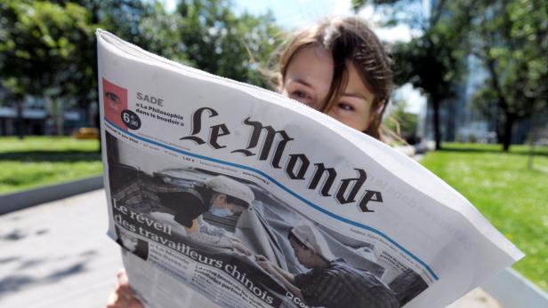 Eine Frau liest die Zeitung „Le Monde“ im Freien.