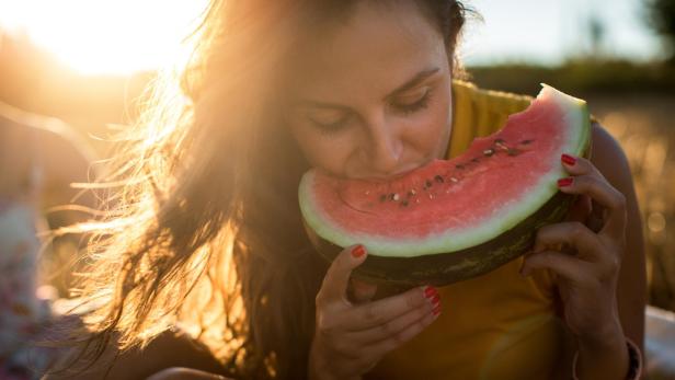 Junge Frau isst im Freien ein Stück Wassermelone.