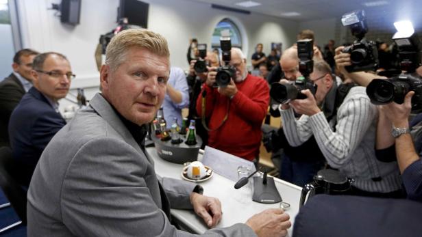 Ein Mann im grauen Anzug sitzt vor einer Gruppe von Fotografen.