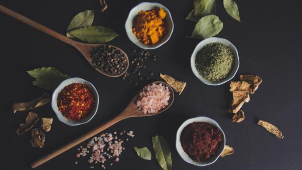 Verschiedene Gewürze und Kräuter sind dekorativ auf einer schwarzen Oberfläche angeordnet.