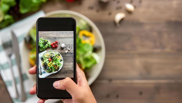 Hand holding smartphone taking photo of beautiful food, mix fresh green salad