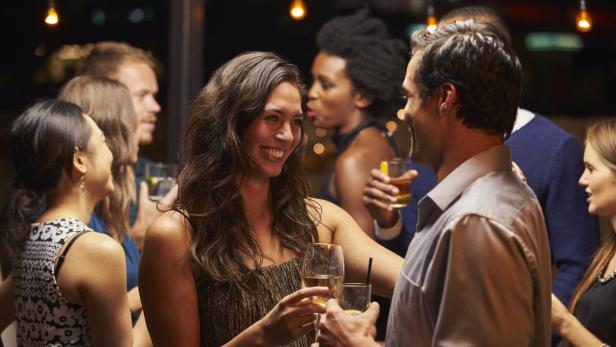 Eine Frau lächelt einen Mann auf einer Party an und hält ein Glas Wein.