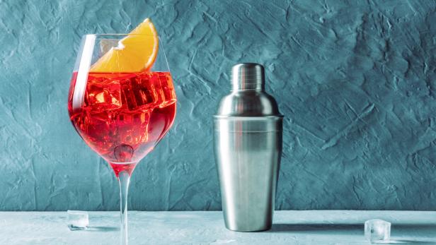 Ein Aperol Spritz mit einer Orangenscheibe und einem Cocktailshaker.