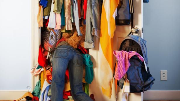 Eine Person klettert in einen überfüllten Kleiderschrank.