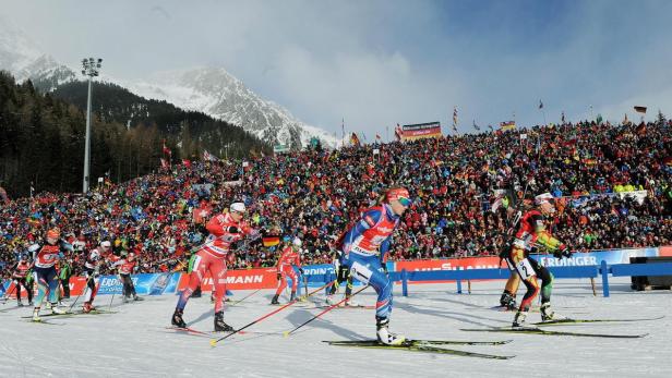 Biathleten starten vor einer großen Zuschauermenge in einem verschneiten Stadion.