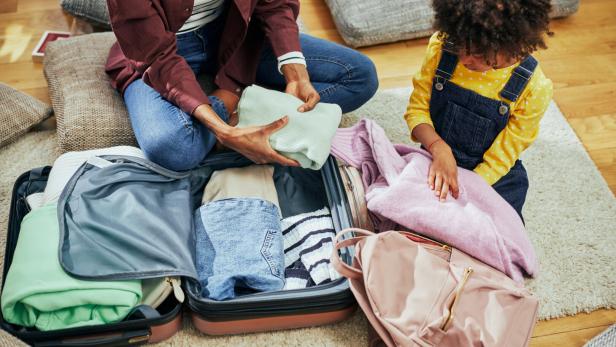 Little African American girl helping her mother pack her suitcase