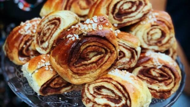 Eine Person hält einen Teller mit Zimtschnecken, die mit Hagelzucker bestreut sind.