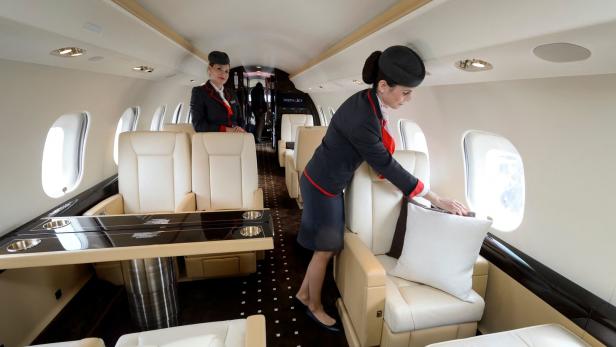 Im Passagierbereich eines Privatjets richtet eine Flugbegleiterin ein Kissen auf einem Sitz zurecht. 