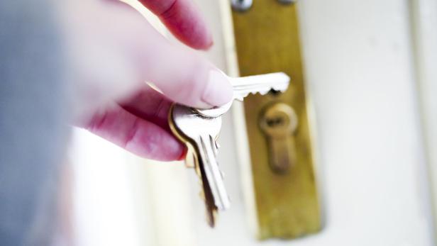Hand mit Schlüssel beim Aufsperren einer Wohnungstüre.