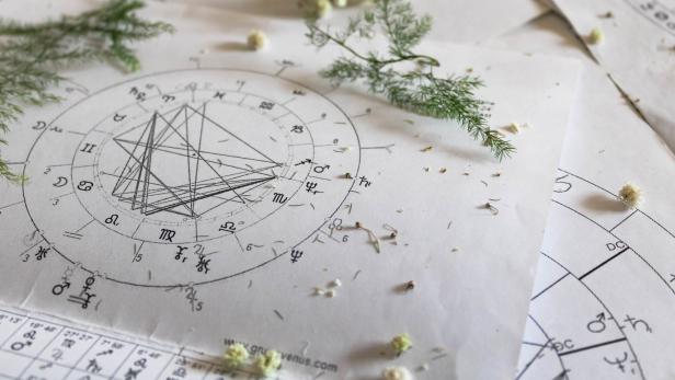 Ein Horoskop-Diagramm liegt auf einem Tisch, dekoriert mit kleinen Blumen und Zweigen.