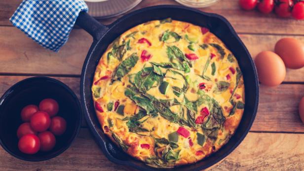 Eine Frittata mit Gemüse in einer gusseisernen Pfanne auf einem Holztisch.