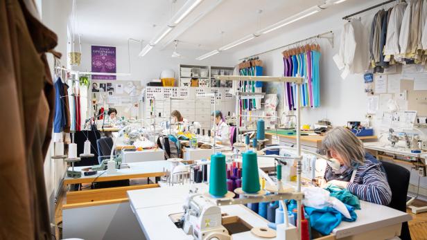 Mehrere Schneiderinnen arbeiten in einer hellen Werkstatt an ihren Nähmaschinen.