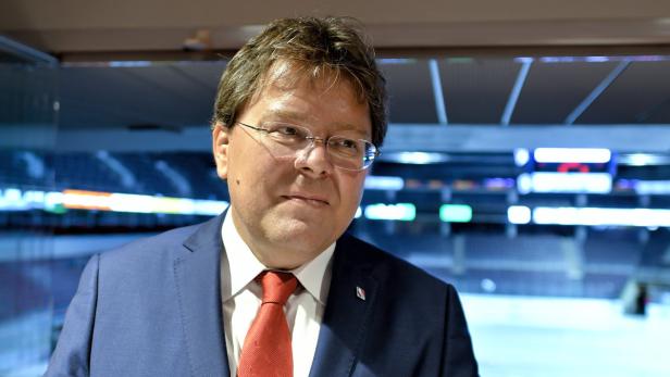 Ein Mann mit Brille und Anzug steht vor einer Eisarena.