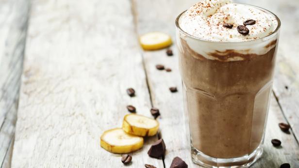 Ein Schokoladen-Bananen-Smoothie mit Schlagsahne und Kaffeebohnen auf einem Holztisch.