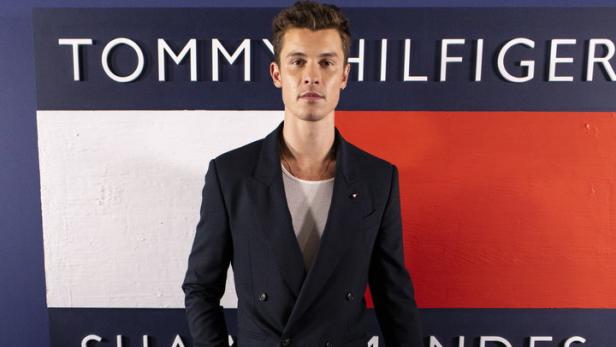 Shawn Mendes posiert vor einem Tommy Hilfiger-Logo.