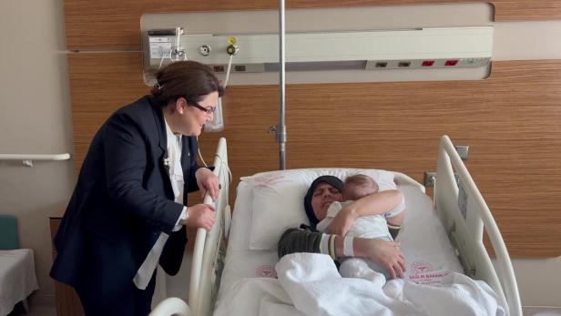 Eine Frau im Anzug besucht eine Mutter mit ihrem Baby im Krankenhaus.