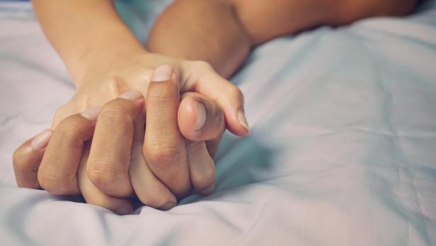 Zwei Hände halten sich auf einem weißen Bettlaken fest.