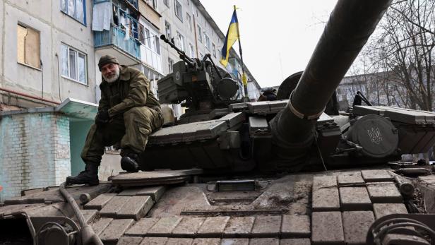 Ein Ukrainer sitzt auf einem Panzer in einer ausgebombten Stadt