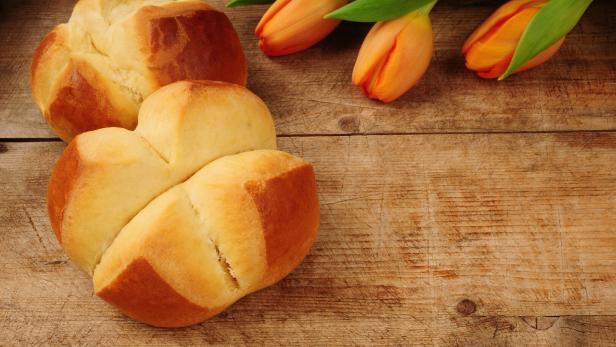 Zwei Brioche-Brote und drei orangefarbene Tulpen auf einem Holztisch.