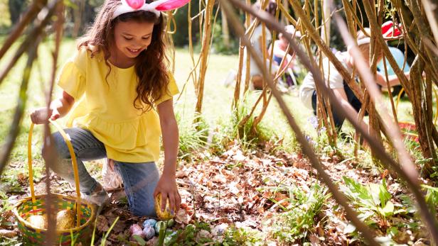 Ein Mädchen mit Hasenohren findet Ostereier bei einer Ostereiersuche.