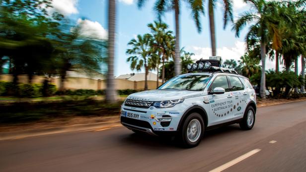 Ein Land Rover Discovery, ausgestattet für eine „Experience Tour Australia 2015“, fährt auf einer Straße mit Palmen.
