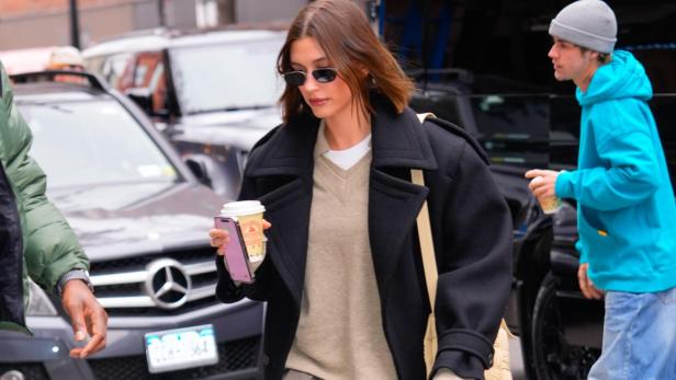 Hailey Bieber mit Sonnenbrille, Mantel und Kaffee auf der Straße.