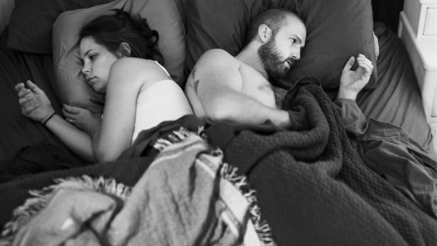 Ein Paar liegt Rücken an Rücken in einem Bett unter einer Decke.