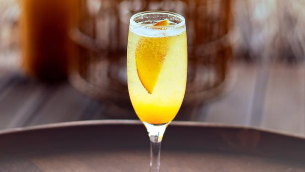 Ein Glas Sekt mit einem Pfirsichstück auf einem Holztablett.