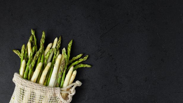 Grüner und weißer Spargel in einem Stoffbeutel auf schwarzem Hintergrund.