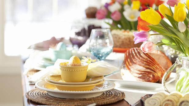 Ein festlich gedeckter Tisch mit Osterschinken, Tulpen und bunten Eiern.