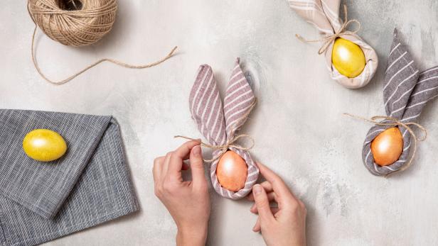 Hände binden ein Osterei in ein Tuch, um es wie ein Häschen aussehen zu lassen.