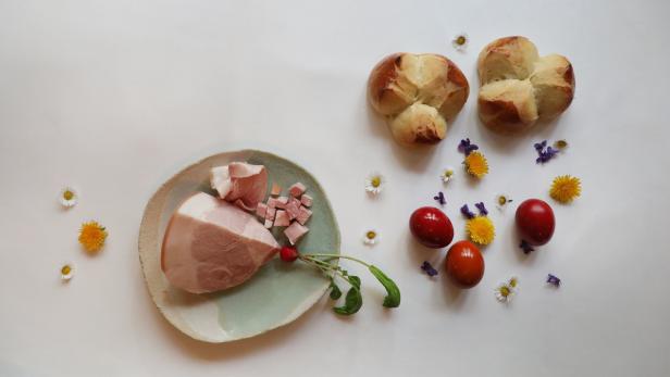 Ein Teller mit Schinken, Krainerwurst, Eiern und Osterbrot, dekoriert mit Blumen.