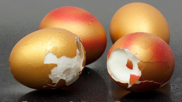 Mehrere goldene und rot-goldene Eier, von denen einige aufgebrochen sind.