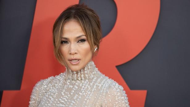 Jennifer Lopez in einem mit Pailletten besetzten Kleid vor einem roten Hintergrund.