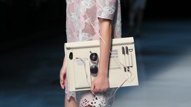 Eine Person hält eine weiße Clutch mit Fächern für Stifte, ein Handy und eine Sonnenbrille.