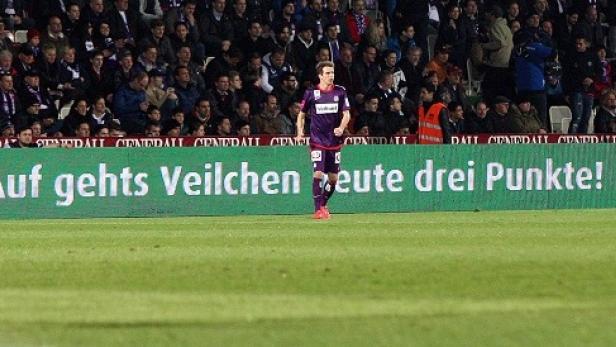 Ein Fußballspieler auf dem Feld vor einer Werbetafel mit der Aufschrift „Auf gehts Veilchen heute drei Punkte!“.