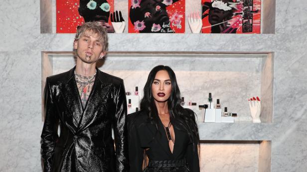 Machine Gun Kelly und Megan Fox posieren zusammen vor einer Marmorwand mit Kunst und Produkten.