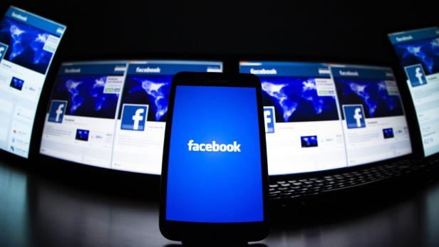 Ein Smartphone zeigt das Facebook-Logo vor mehreren Computerbildschirmen mit der Facebook-Webseite.