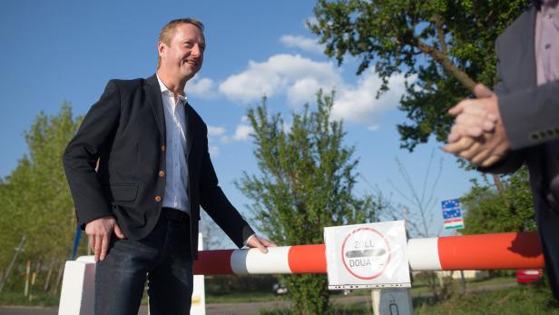 Ein Mann in Jackett steht an einer Zollschranke.