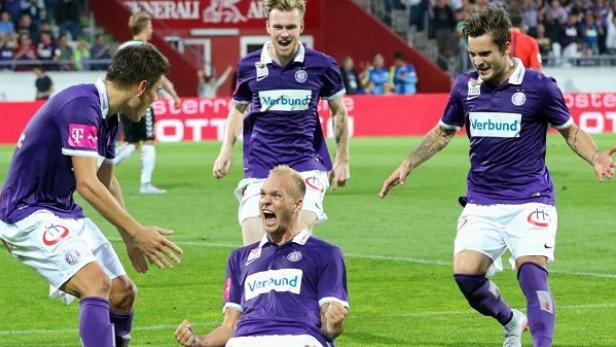 Mehrere Fußballspieler in lila Trikots jubeln auf dem Spielfeld.