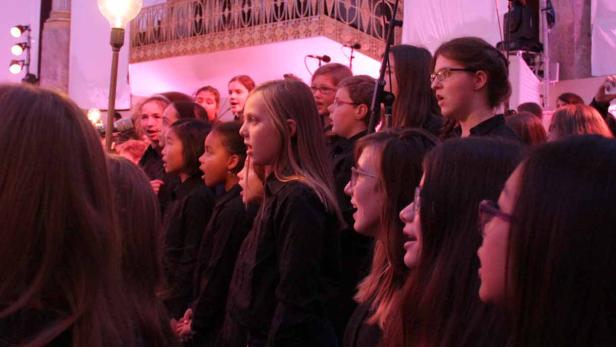 Ein Kinderchor singt auf einer Bühne mit rosa Beleuchtung.