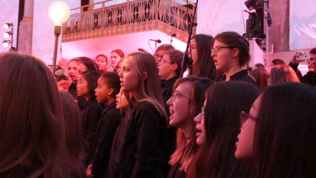 Ein Jugendchor singt auf einer Bühne mit roter Beleuchtung.