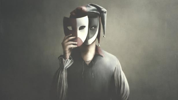 Eine Person mit Narrenkappe hält eine Maske vor ihr Gesicht.